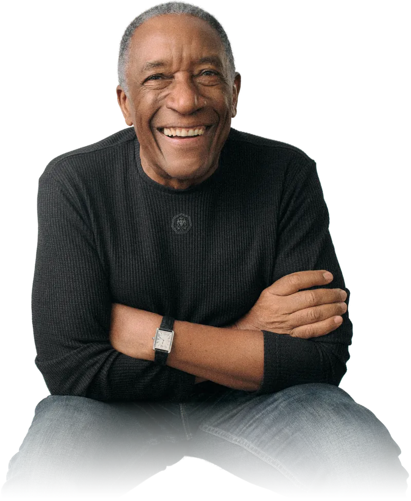 Geraldo Rufino sorrindo, sentado, de braços cruzados.